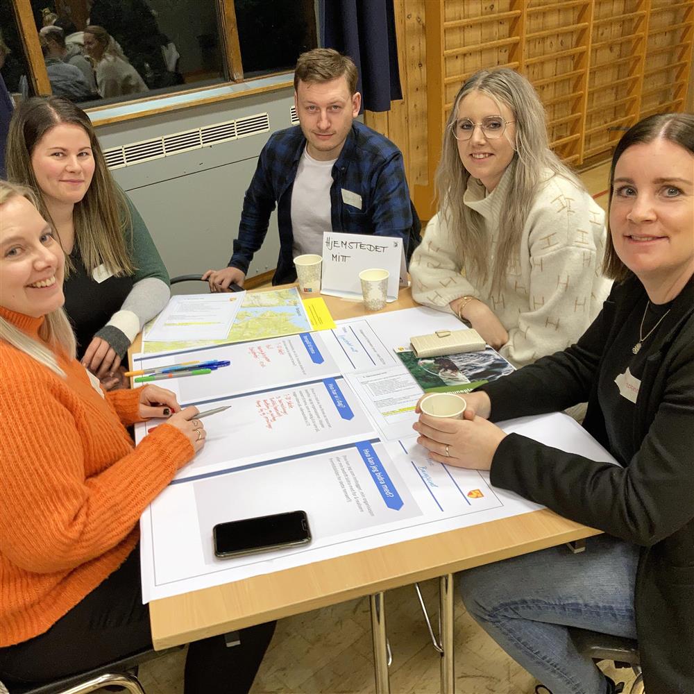 Mennesker samlet til møte, sittende rundt forskjellige bord, eller stående. Folk snakker sammen, mens andre lytter. - Klikk for stort bilde